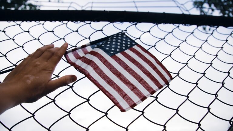 American Flag in hand attached to a chain link fence